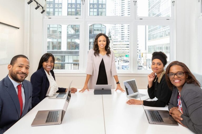 Diverse group of business professionals seated around a conference table with laptops in a bright office